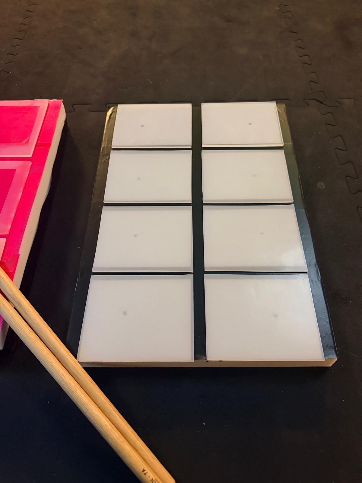Prototype à huit pads blancs posé au sol, à côté d’une paire de baguettes.